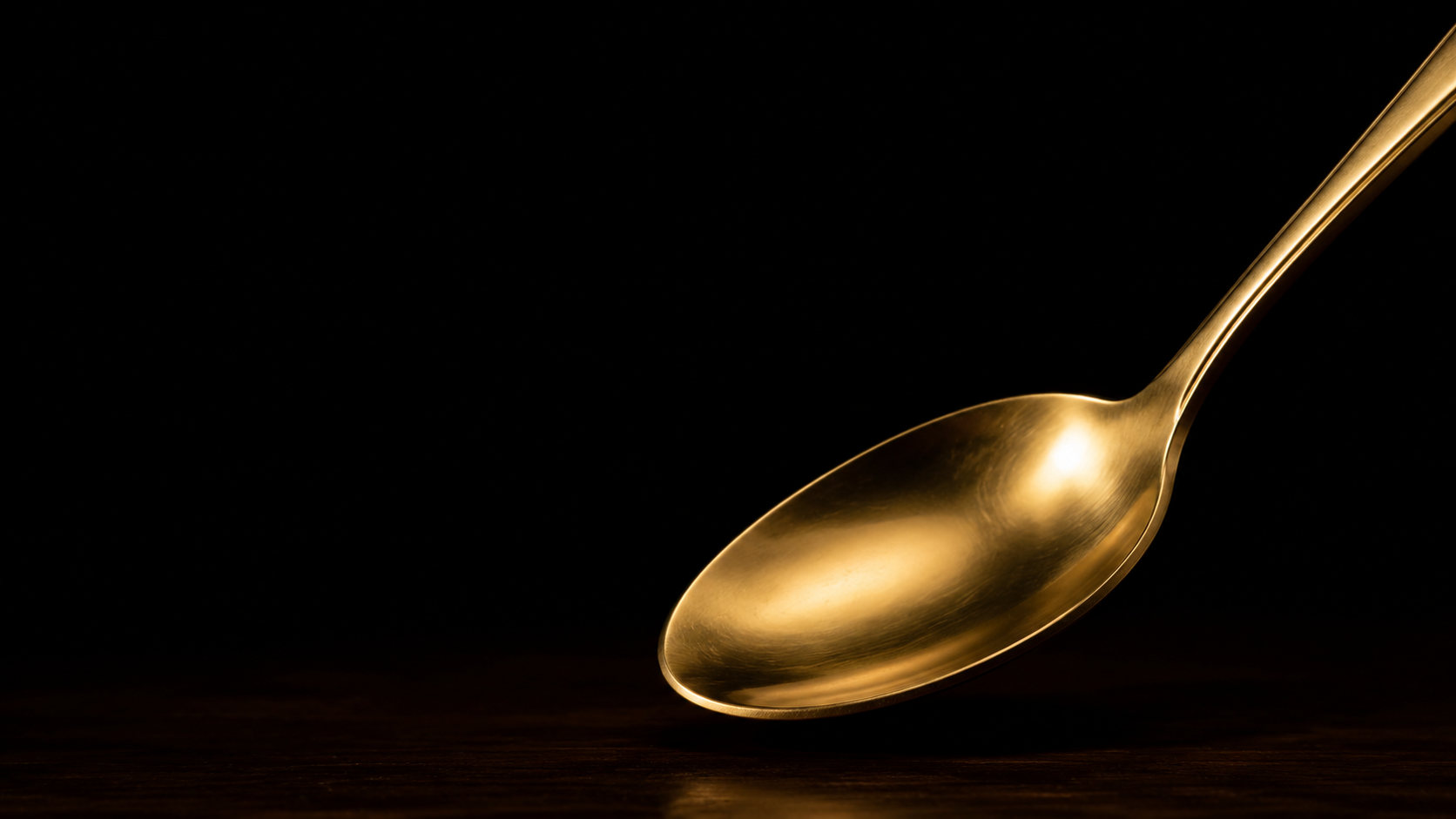 Goldener Löffel vor tiefschwarzem Hintergrund